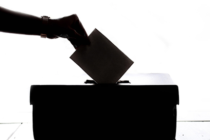 Person hand holding a ballot and dropping it into a ballot box.